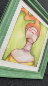 Acquerello con atmosfera sognante che raffigura una donna con i capelli Rossi col viso alzato verso il cielo, la cornice restaurata riprende i colori dell’illustrazione